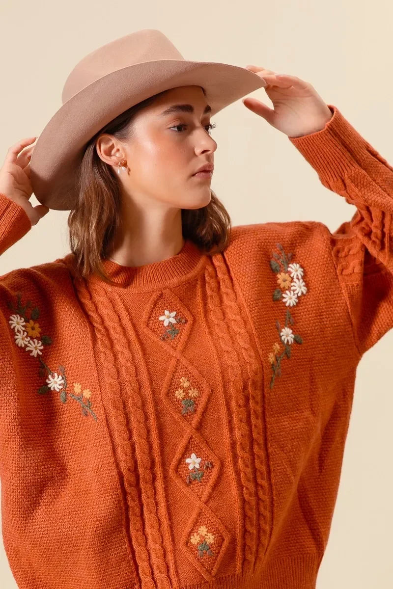Rustic orange cable knit sweater with floral embroidery, paired with a wide-brim hat for boho style